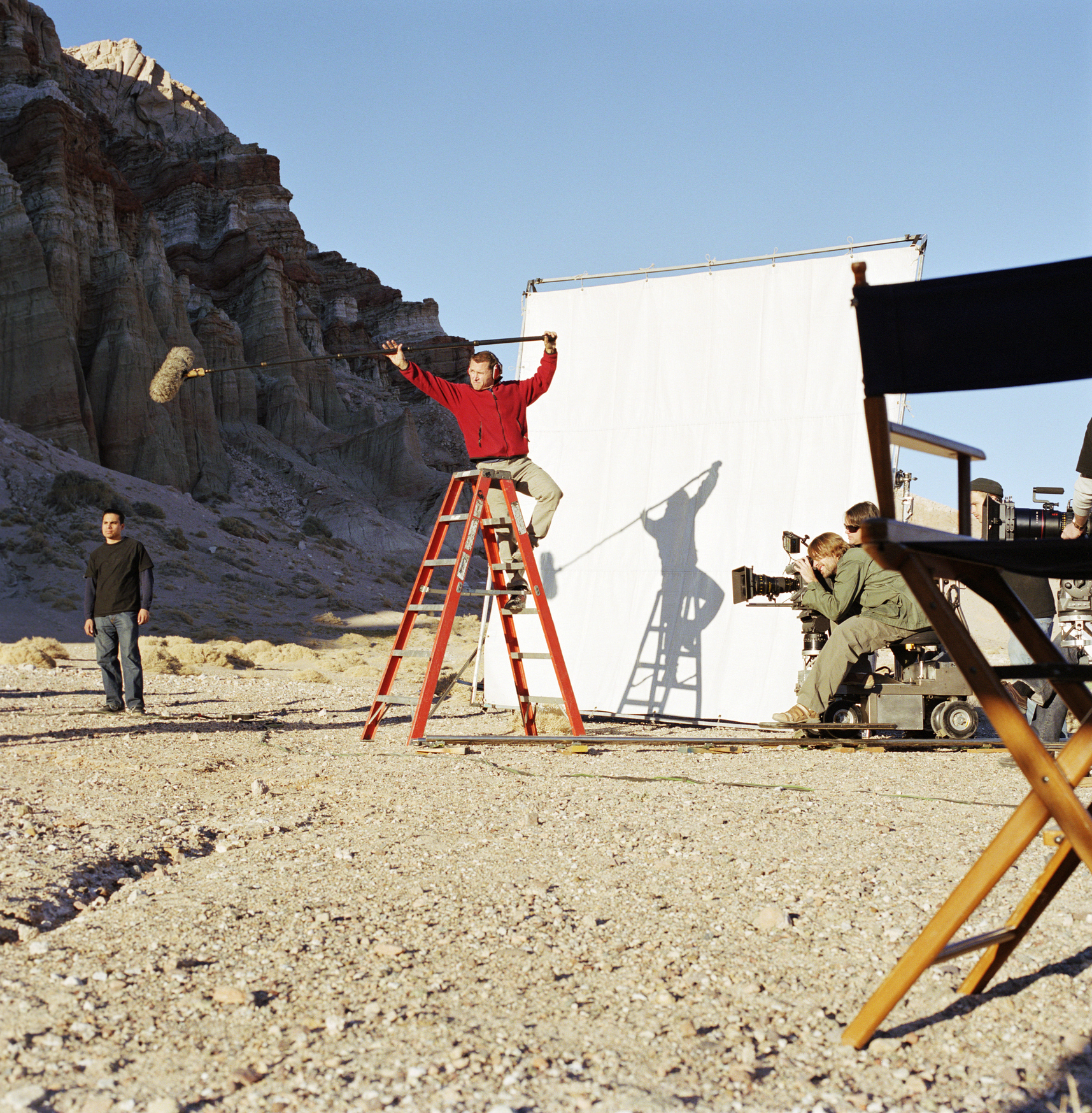 A boom operator on a ladder holding a microphone over a desert film set