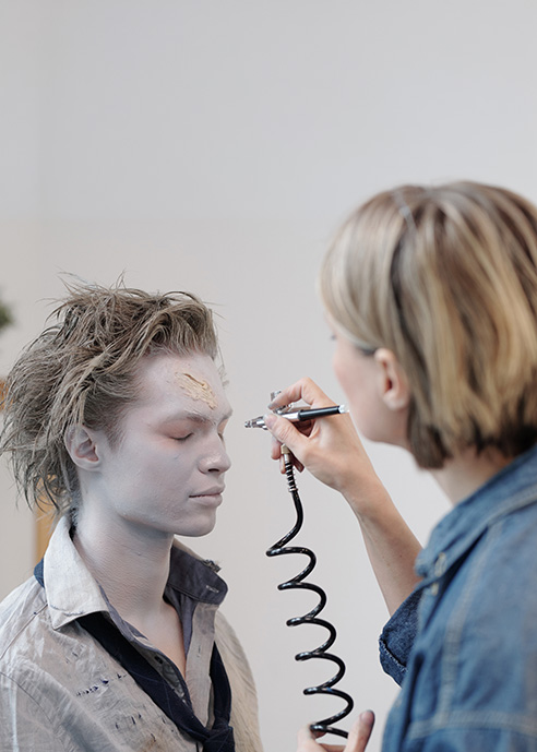 Artist applying airbrush makeup to a performer during special effects makeup preparation.