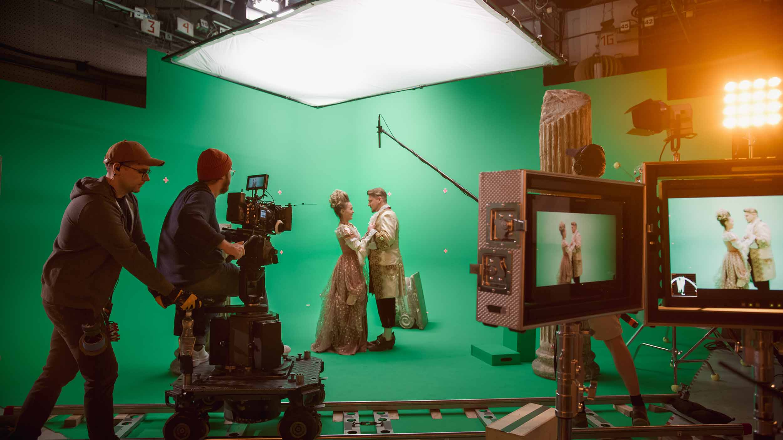 A film crew filming two actors in period costume on a green-screen soundstage