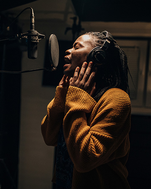 Person wearing headphones speaking into a microphone in a recording studio.