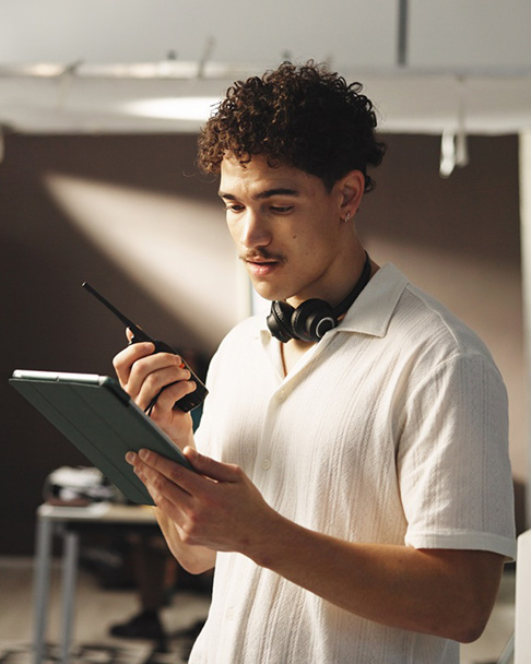 Production team member reviewing a digital tablet while communicating via handheld radio on a film set.