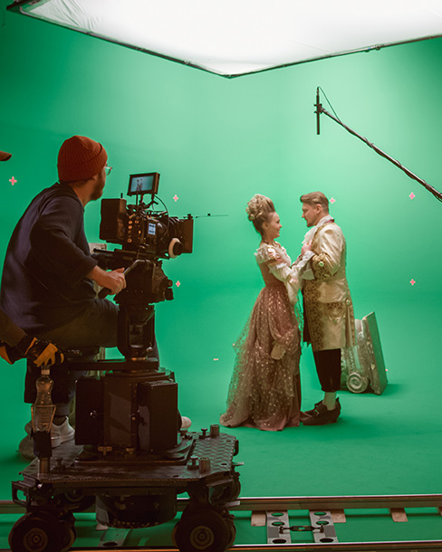 Camera operator filming performers on a green screen stage for visual effects production.