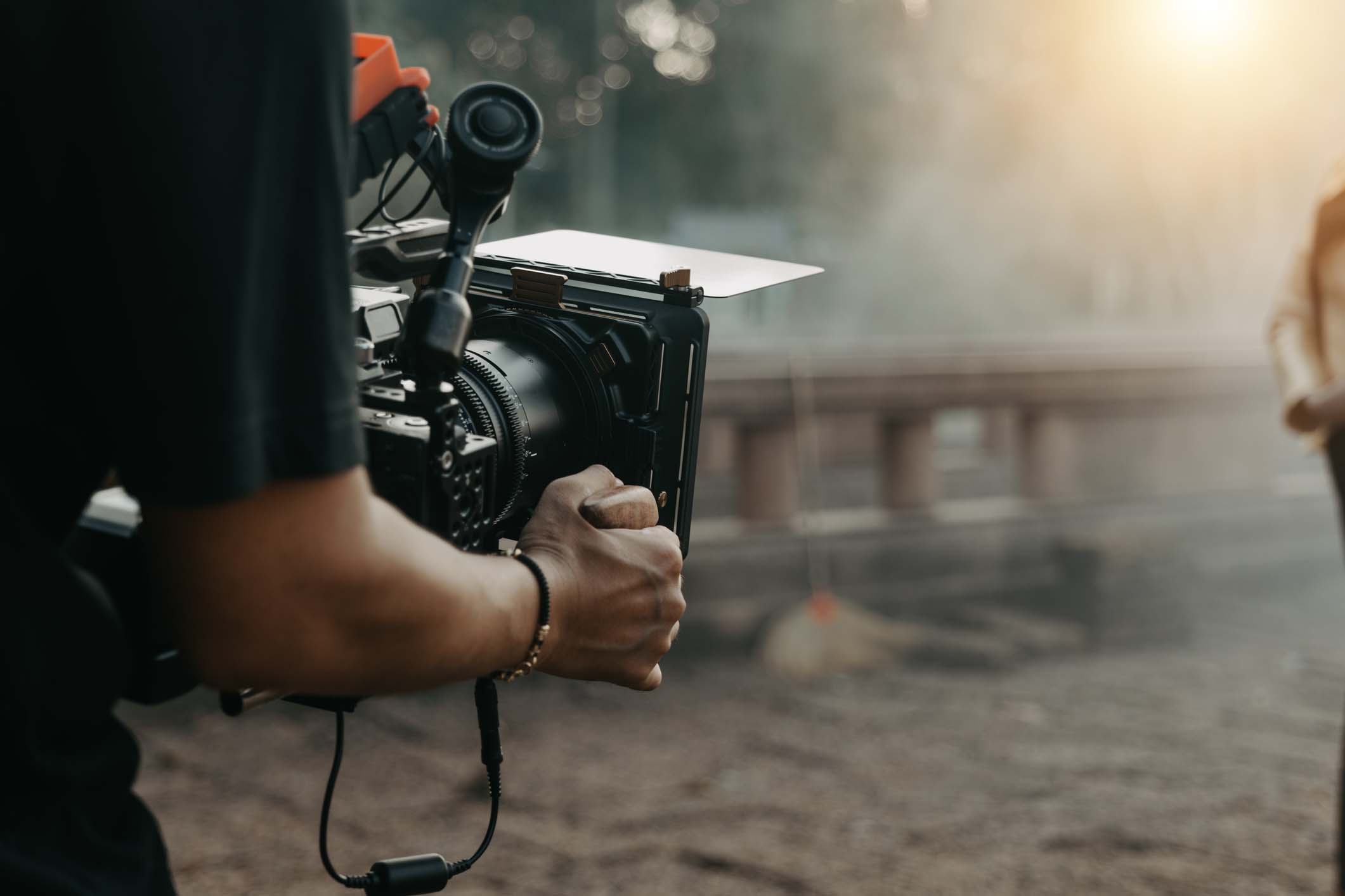 A camera operator holding a cinema camera on location, hands and equipment in soft focus
